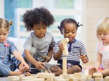 A multi-ethnic group of toddlers are sitting together on the floor holding playing with wood blocks together.